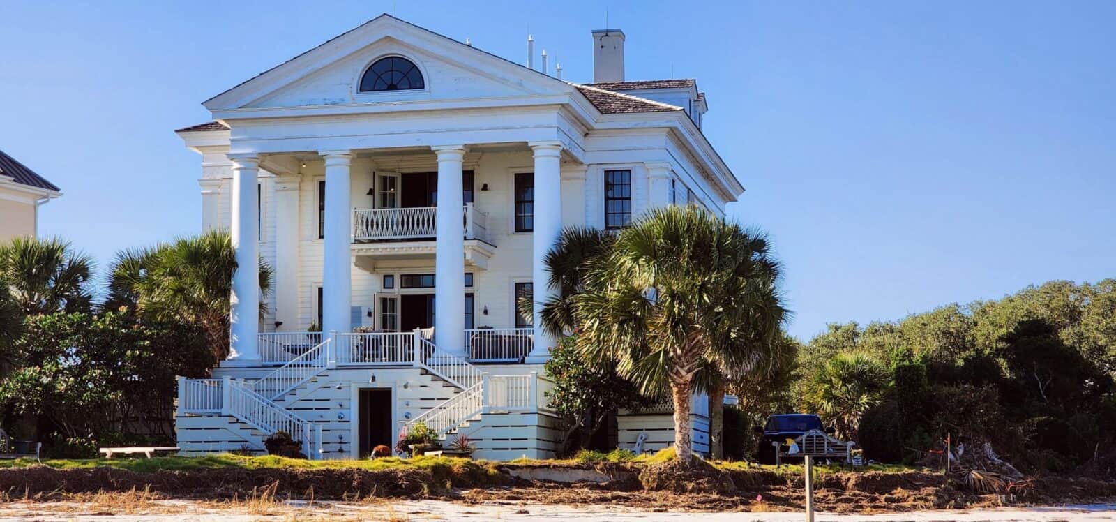 Beautiful white coastal house with columns and palm trees in front.