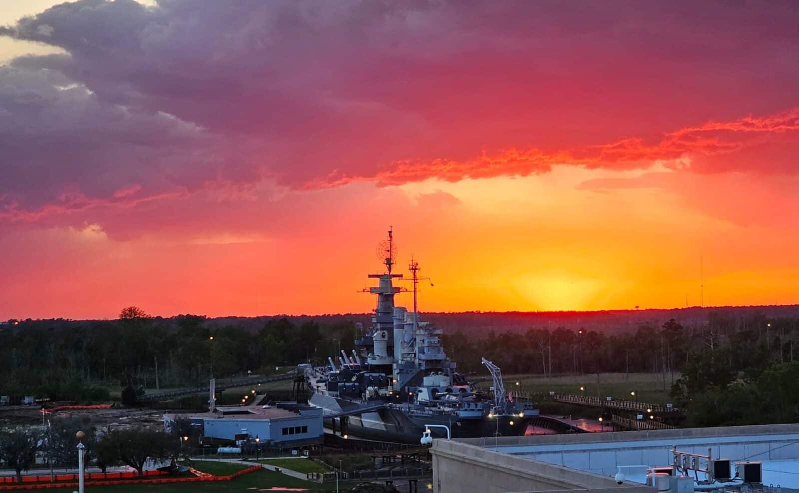 Vivid sunset with orange and pink hues over a navy shipyard and ships.