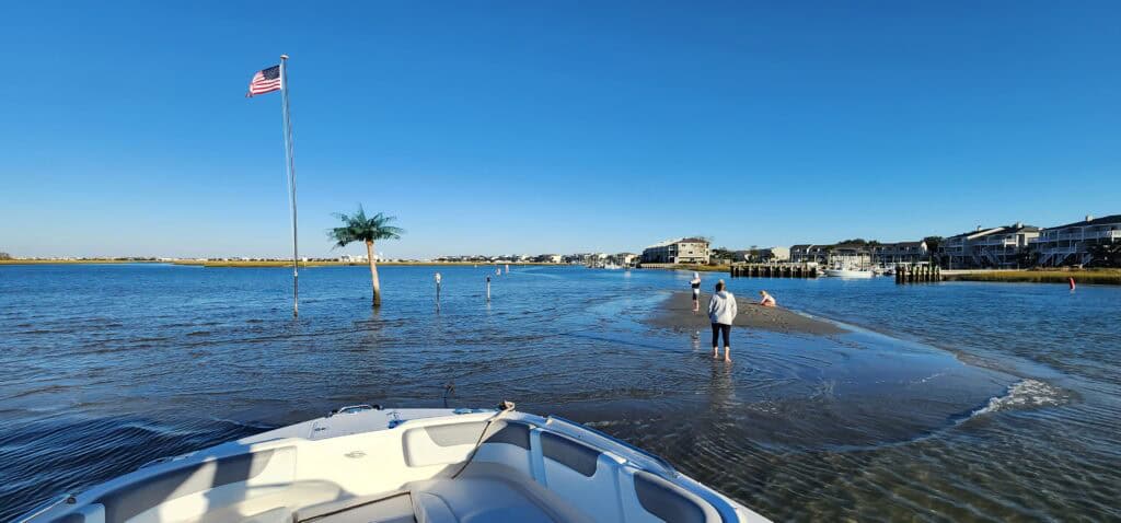 Person walking on shoreline with boat in foreground and American flag in background.