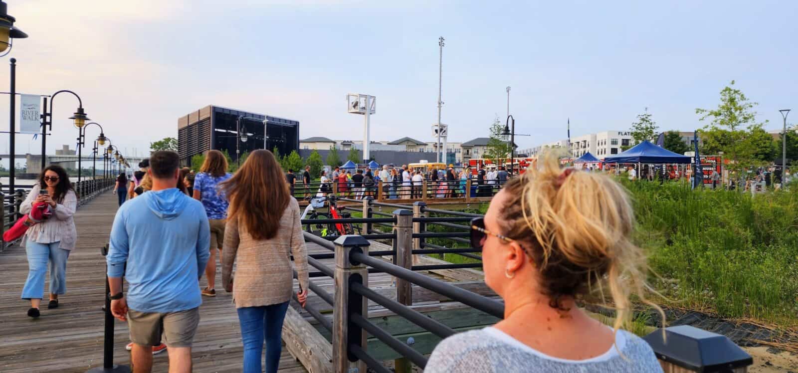 People walking along a waterfront park with benches and greenery.