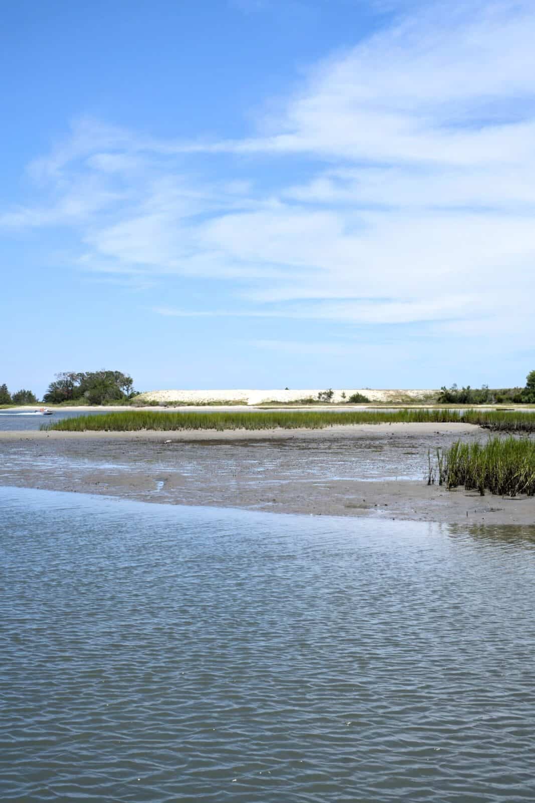 Salt marsh and tidal flats with a sandbar and grasses under a blue sky in the Masonboro / Greenville Loop area of Wilmington, NC.