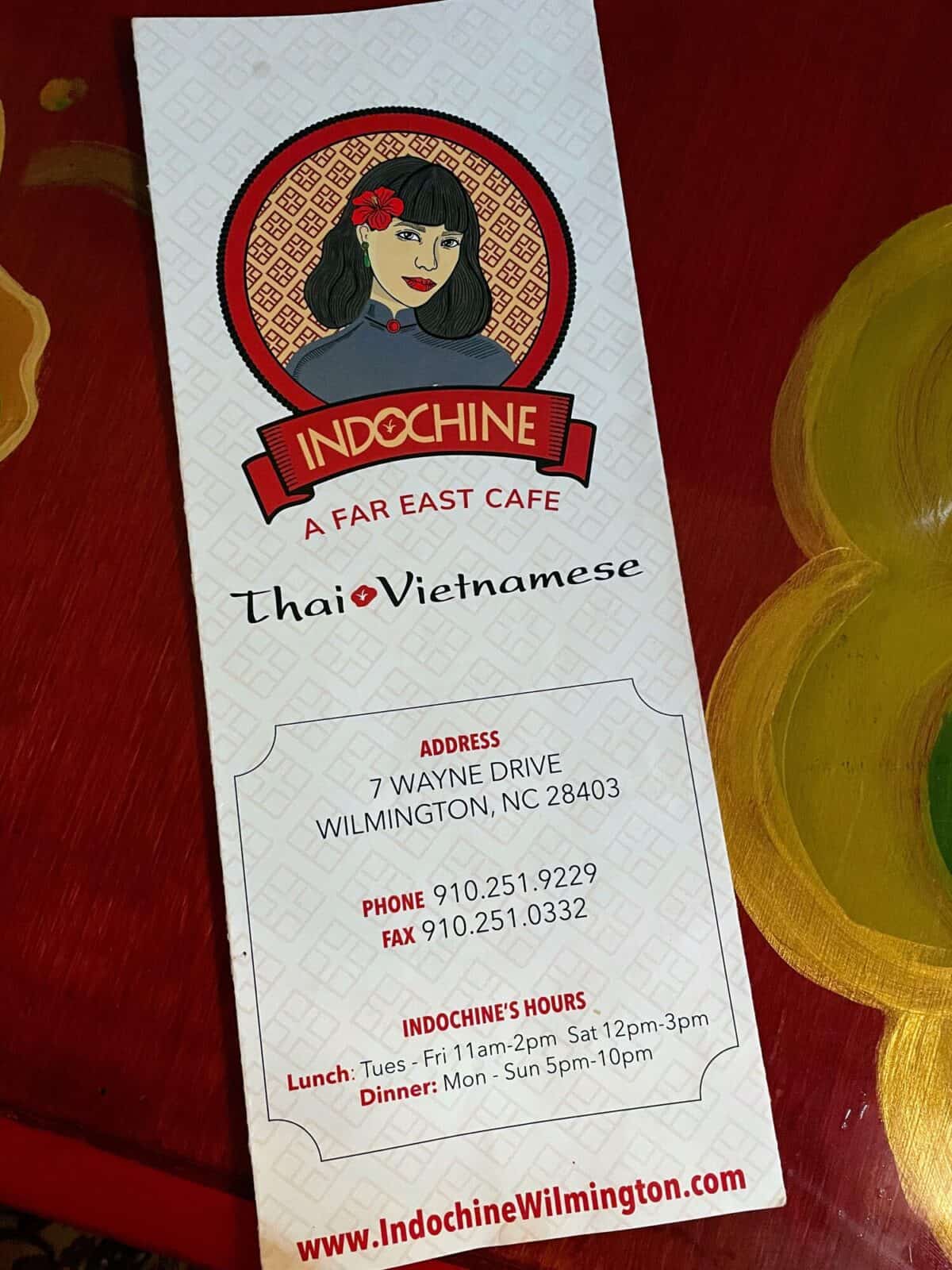 An Indochine restaurant menu resting on a red painted table.