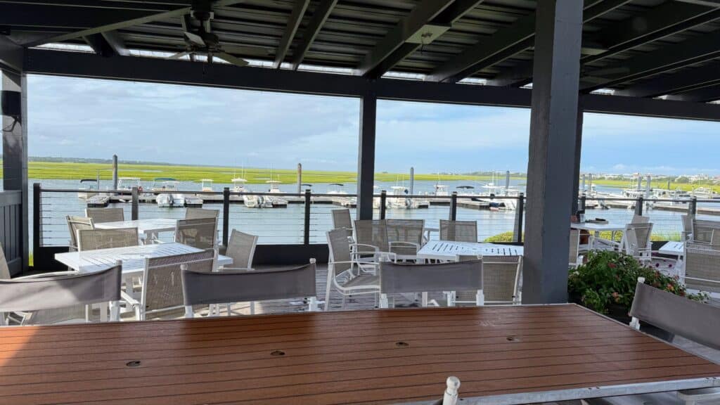Outdoor waterfront dining area with tables and chairs under a covered patio.