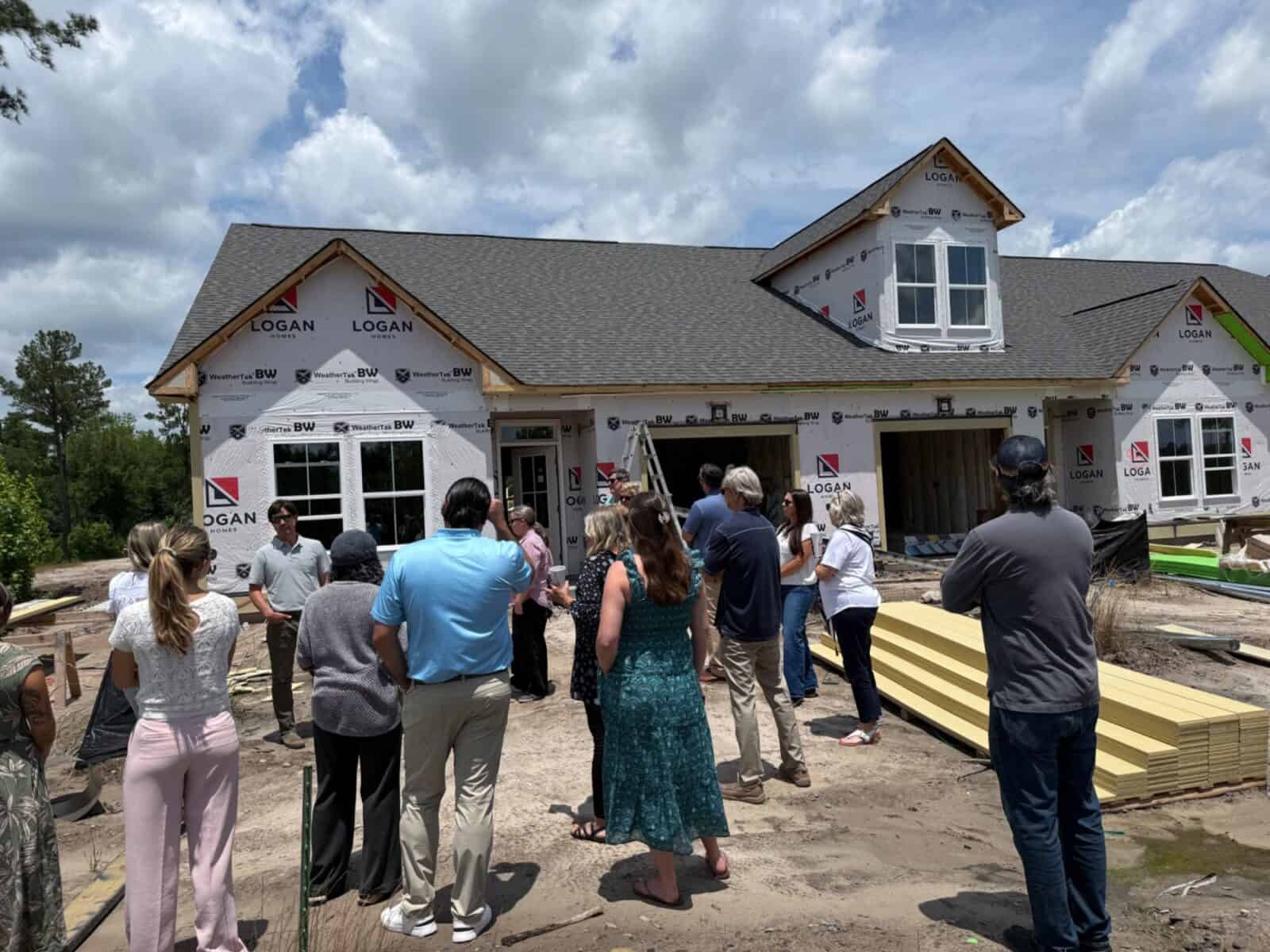 Buyers touring a home under construction wrapped in Logan Homes building paper — a common sight across Leland.