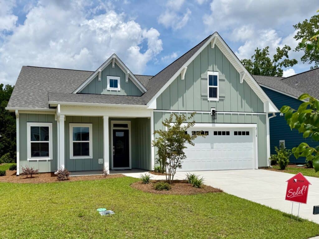Beautiful modern blue house with white trim and a sold sign in the yard.