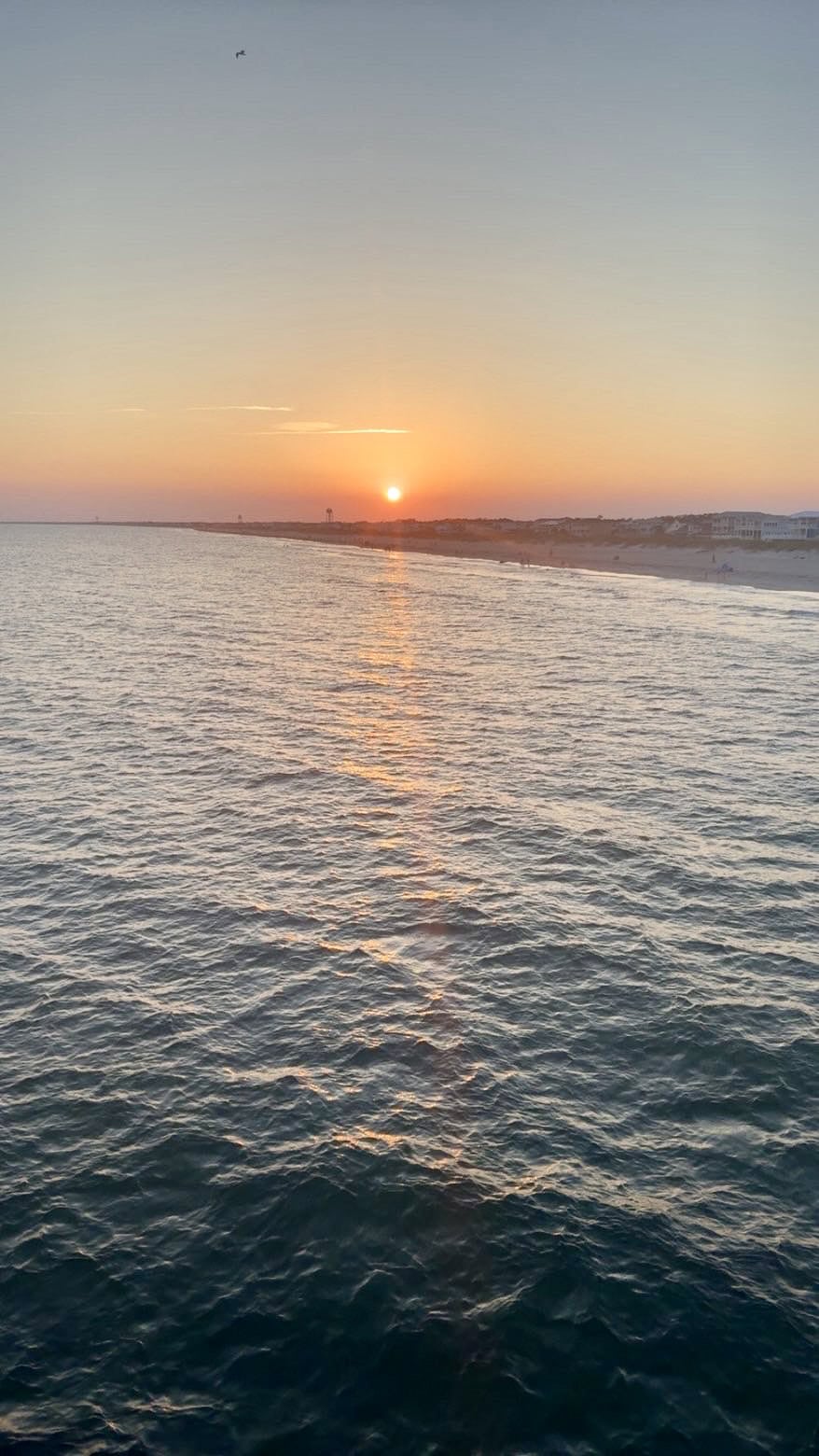 Golden sunset over the Atlantic Ocean with calm water and a distant coastline on the North Carolina coast.