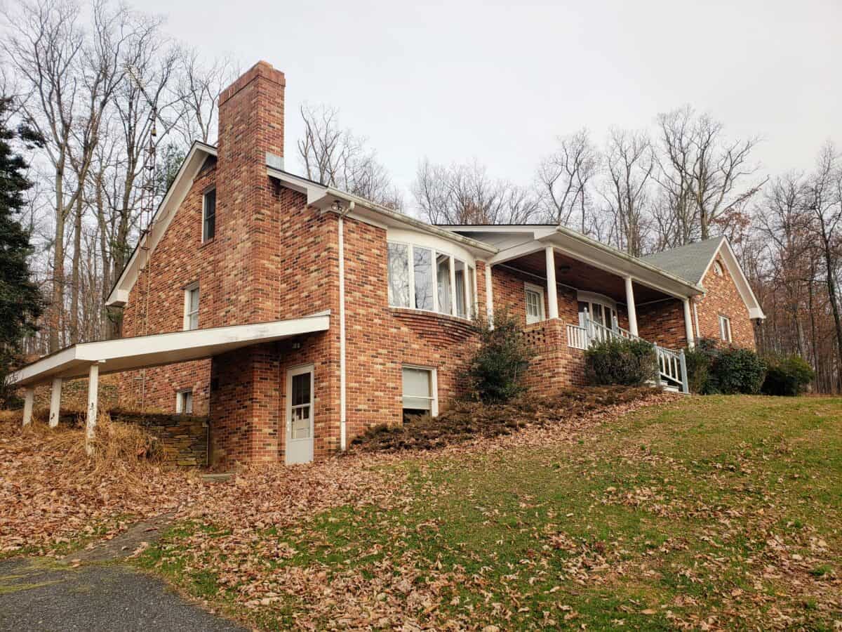 Exterior of our 1970s brick rancher with a covered porch and leaf-covered lawn before the renovation