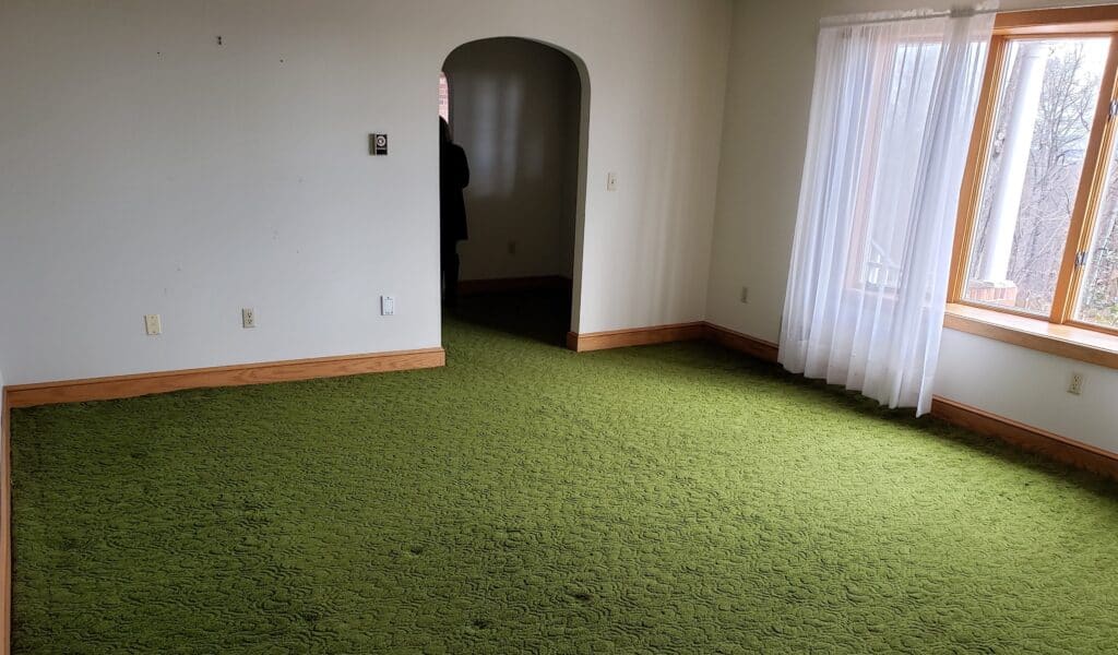 Room before renovation with green carpet and large windows
