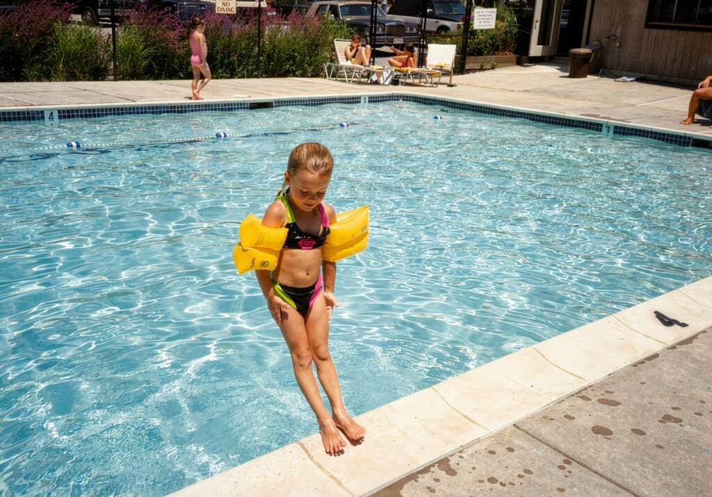 Child with floaties jumping into a backyard swimming pool.
