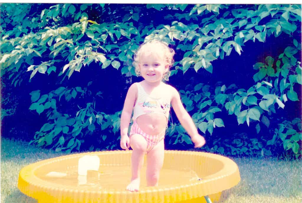 Baby Tabi standing in a yellow baby pool in her grandparents' backyard