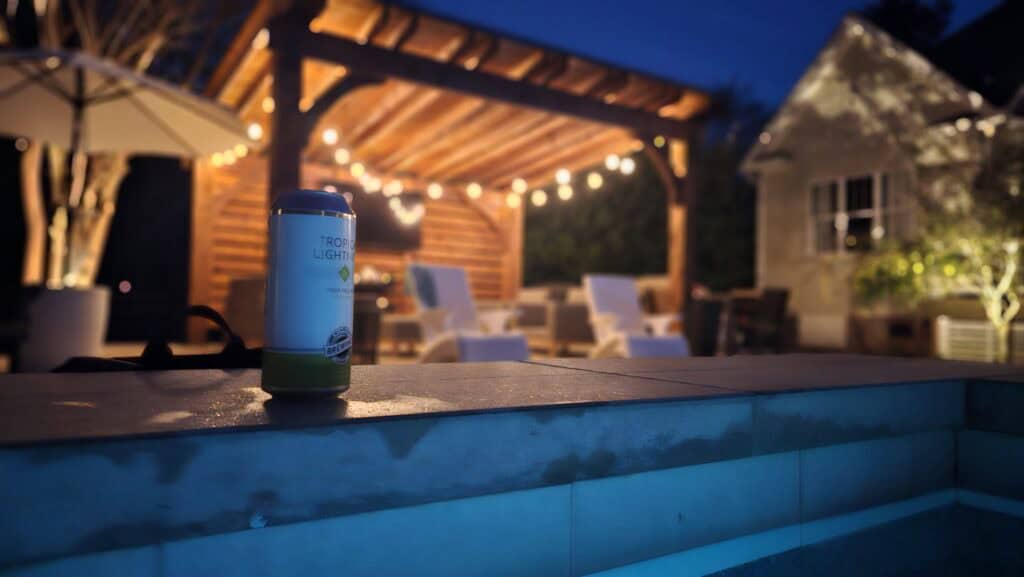 Backyard pool lit up at night with string lights on the pergola