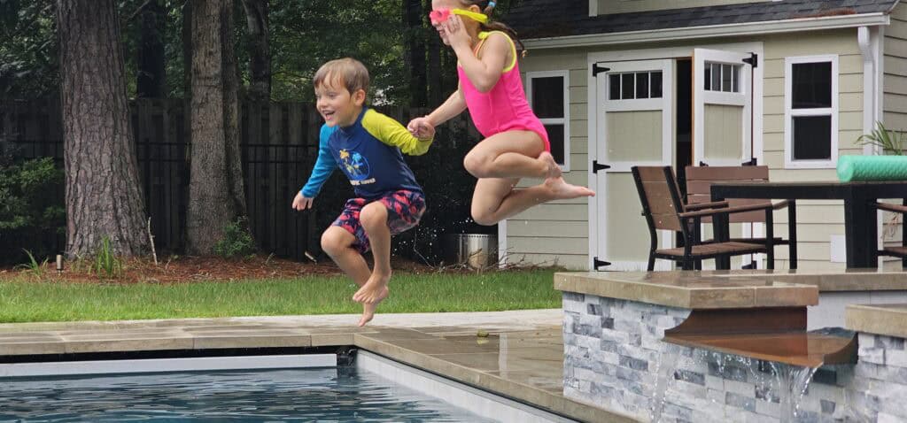 Two kids mid-jump into the backyard pool with huge smiles