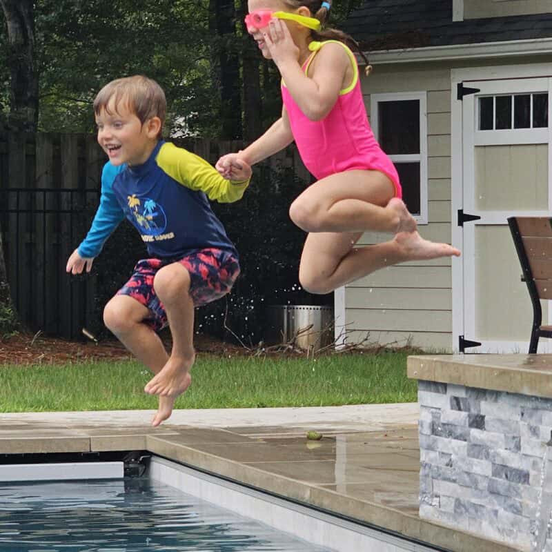 Two kids mid-jump into our backyard pool