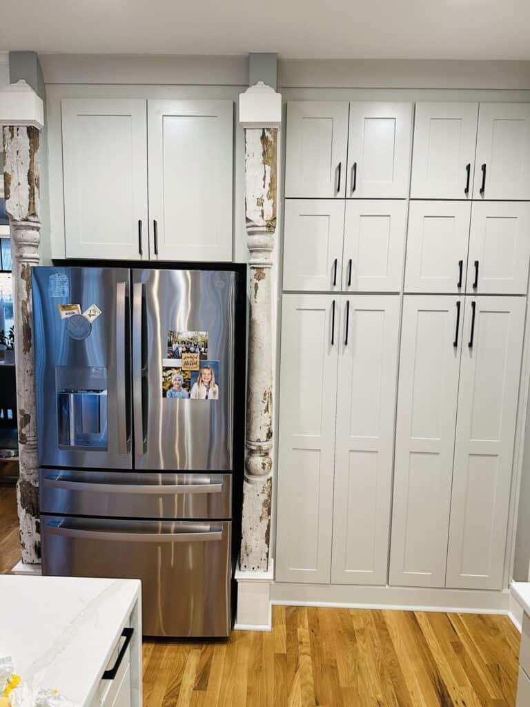 Fridge wall after the remodel with light pantry cabinets and black pulls, keeping the original antique columns