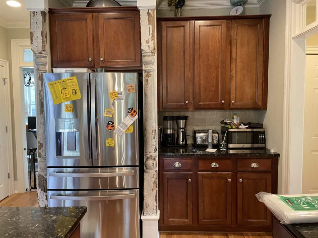 Fridge wall before the remodel with dark wood cabinets and antique chippy white columns