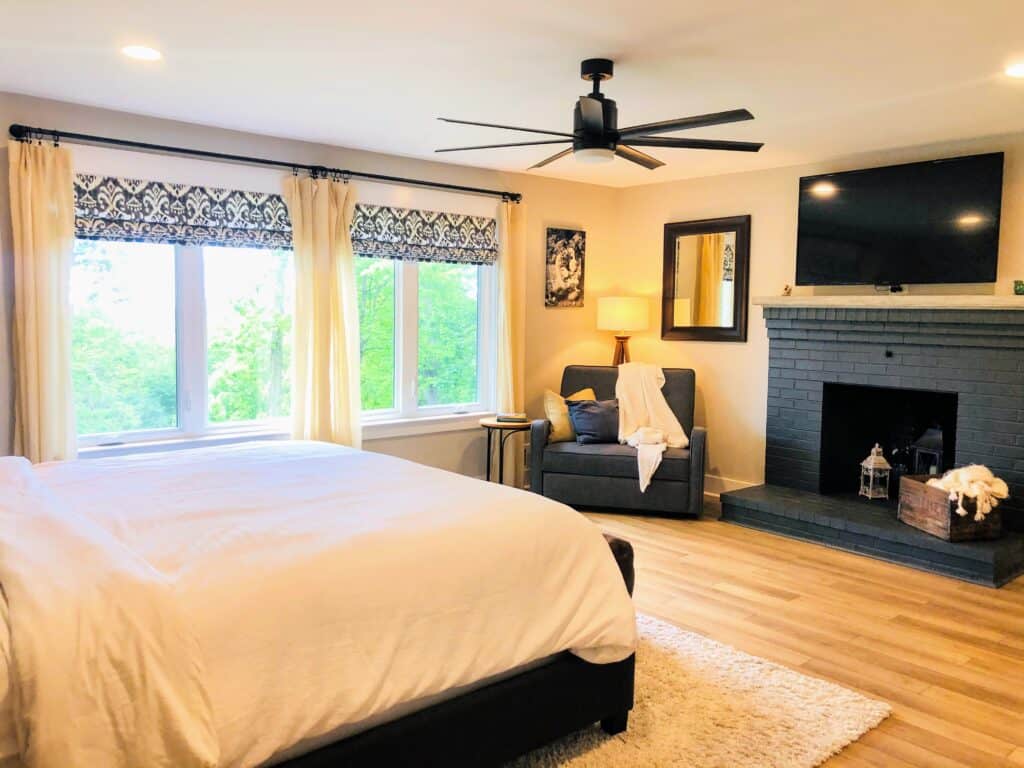 Finished primary bedroom with painted brick fireplace and ceiling fan