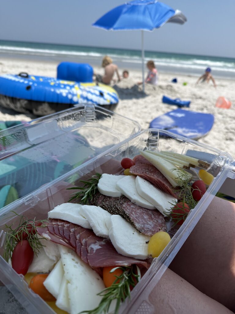 Beach day with a blue umbrella and a snack box on the sand near Wilmington, NC