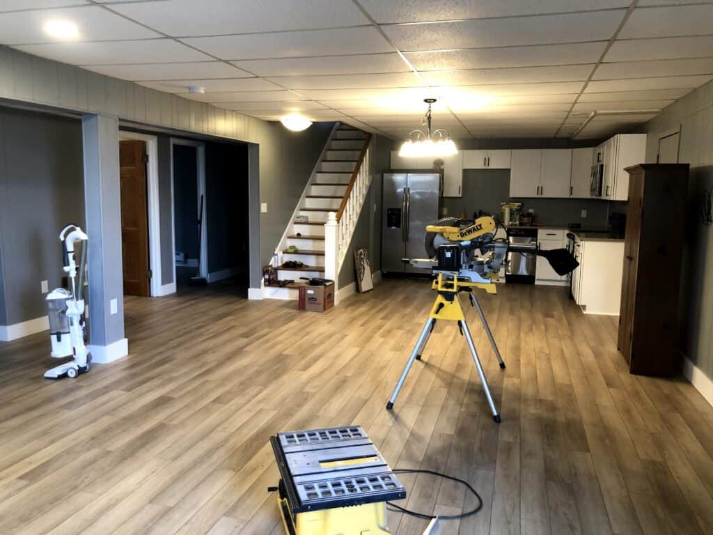 Basement rec room mid-renovation with new wood-look floors and painted walls