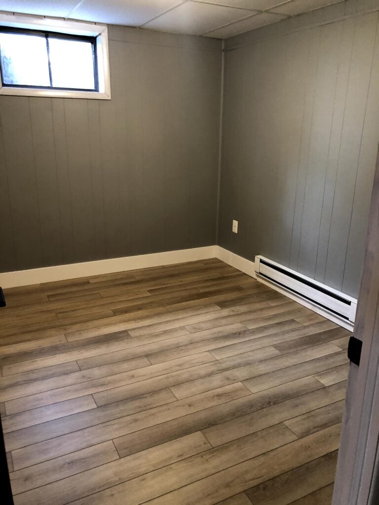 Basement bedroom after renovation with gray walls and wood-look floors