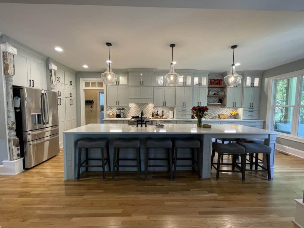 Remodeled Wilmington NC kitchen with light cabinets, a large quartz island with barstools, and three glass pendant lights