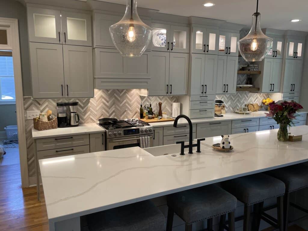 Quartz kitchen island with farmhouse sink and black faucet under glass pendants, with glass-front upper cabinets