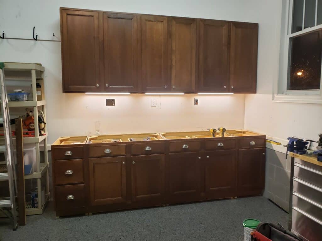 The old dark wood kitchen cabinets reinstalled in the garage with under-cabinet lighting