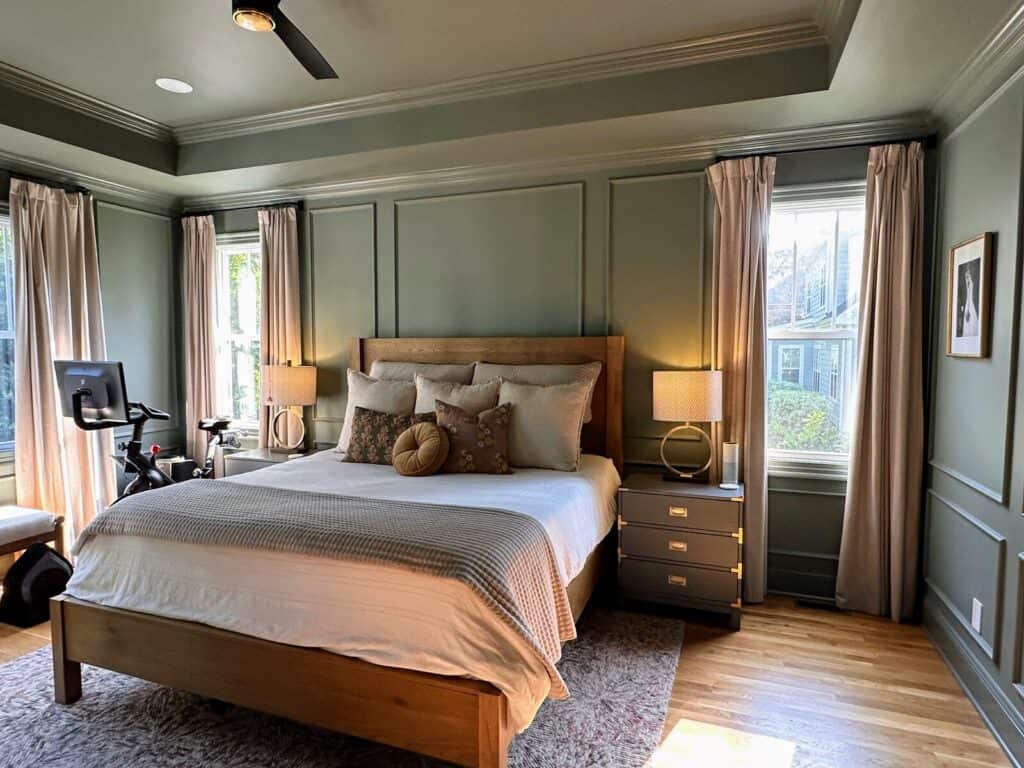 Primary bedroom after the makeover, wide view of the green paneled walls, wood bed and gray nightstands