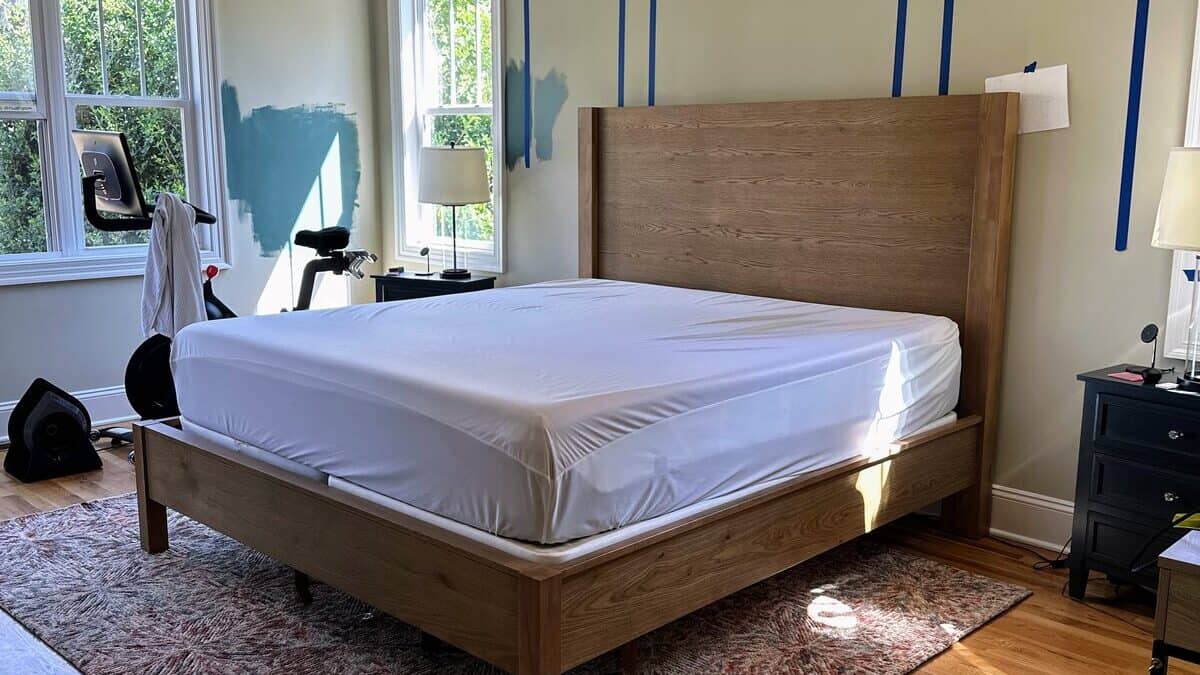 Primary bedroom mid-makeover with blue painter's tape laying out picture-frame molding on the wall behind the bed