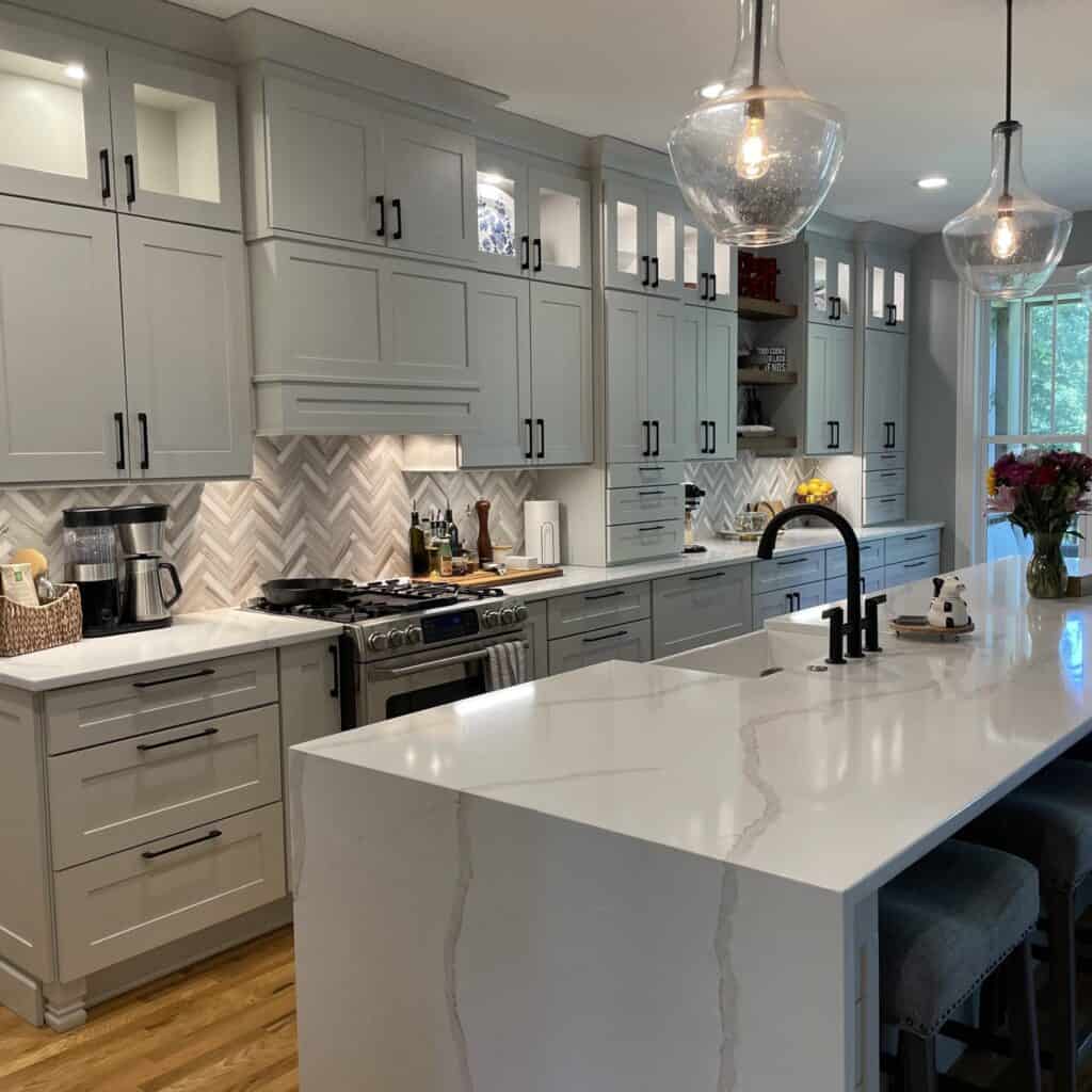 Calacatta Oro quartz island with a waterfall edge and marble herringbone backsplash behind it