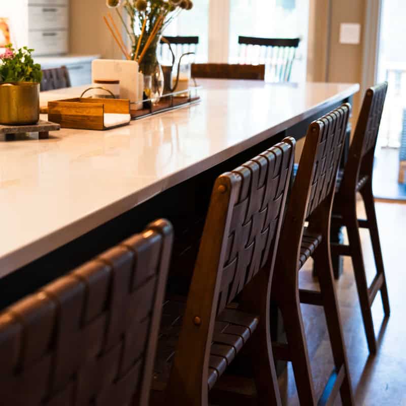 White quartz kitchen island with woven leather barstools and a vase of fresh flowers in a Wilmington NC kitchen designed with Greer Elizabeth Interiors