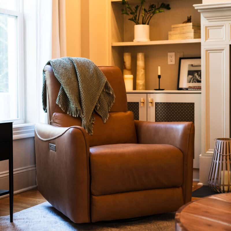 Cognac leather armchair with a knit throw beside white built-in bookshelves in a Wilmington NC living room designed with Greer Elizabeth Interiors