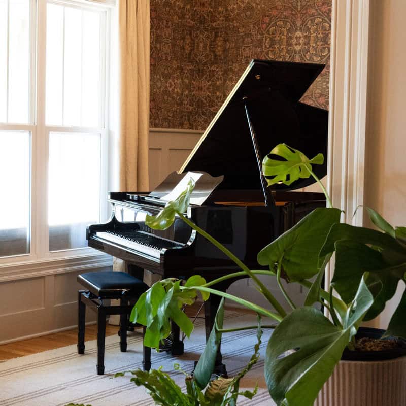 Piano room with patterned wallpaper, a black grand piano, a drum chandelier and floor-length cream curtains in a Wilmington NC home designed with Greer Elizabeth Interiors