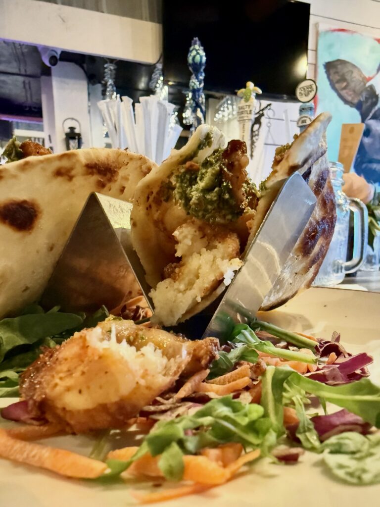 A bitten shrimp and grits taco showing the crispy grit cake inside, with chimichurri, at RumCow in downtown Wilmington NC